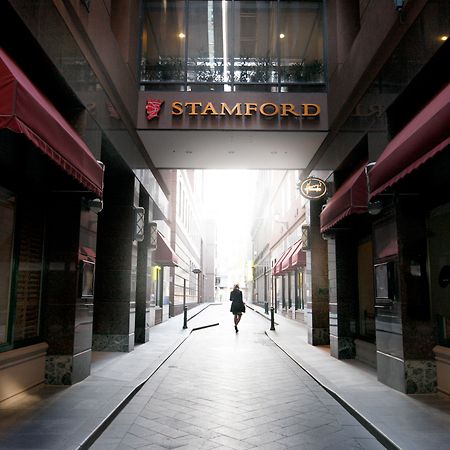 Hotel Stamford Plaza Melburne Exterior foto The photo depicts a narrow alley or passageway, possibly in an urban setting. On one side, there are storefronts with canopies, and on the opposite side, there is a prominent sign reading "STAMFORD." The pathway is lined with buildings, creating a se