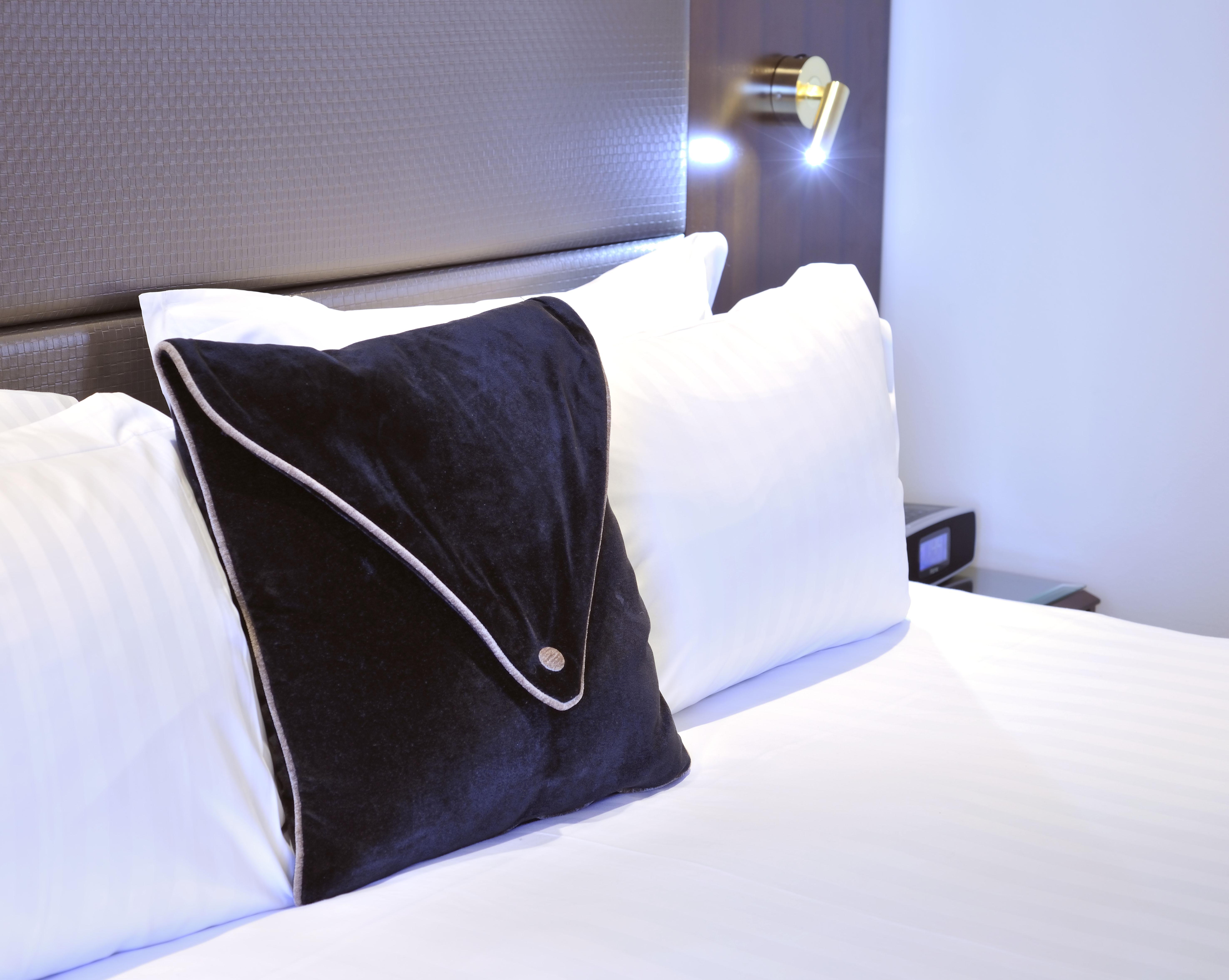 Hotel Stamford Plaza Melburne Exterior foto The photo shows a neatly arranged bed with white linens. There are several pillows, with one black pillow featuring a distinctive design on top of the white pillows. The headboard of the bed is visible, along with a stylish wall-mounted light fixture