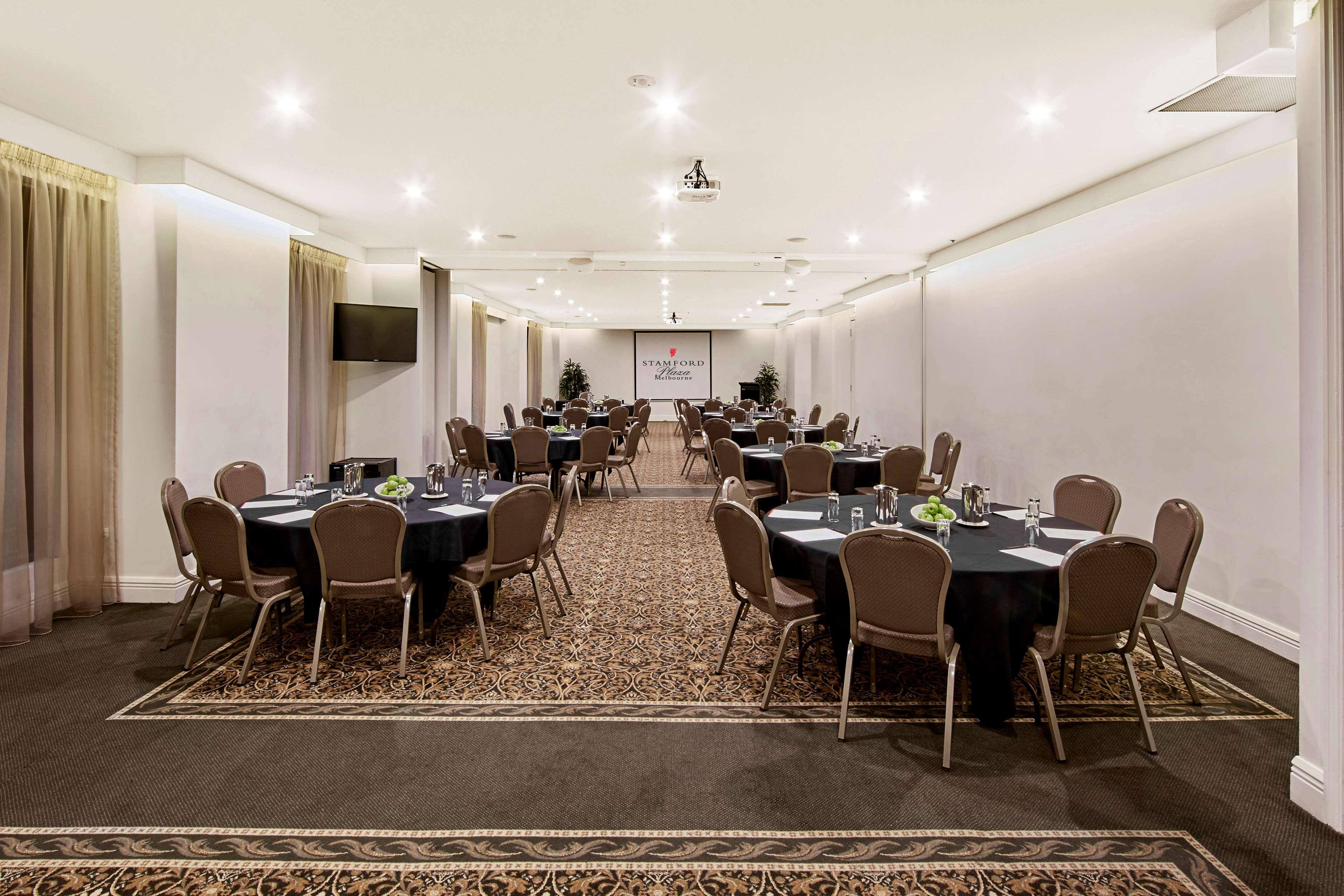 Hotel Stamford Plaza Melburne Exterior foto The photo shows an event space or banquet hall set up for a gathering. The room features several round tables covered with black tablecloths, each adorned with small centerpieces. Chairs are arranged around each table. The lighting is bright and mode