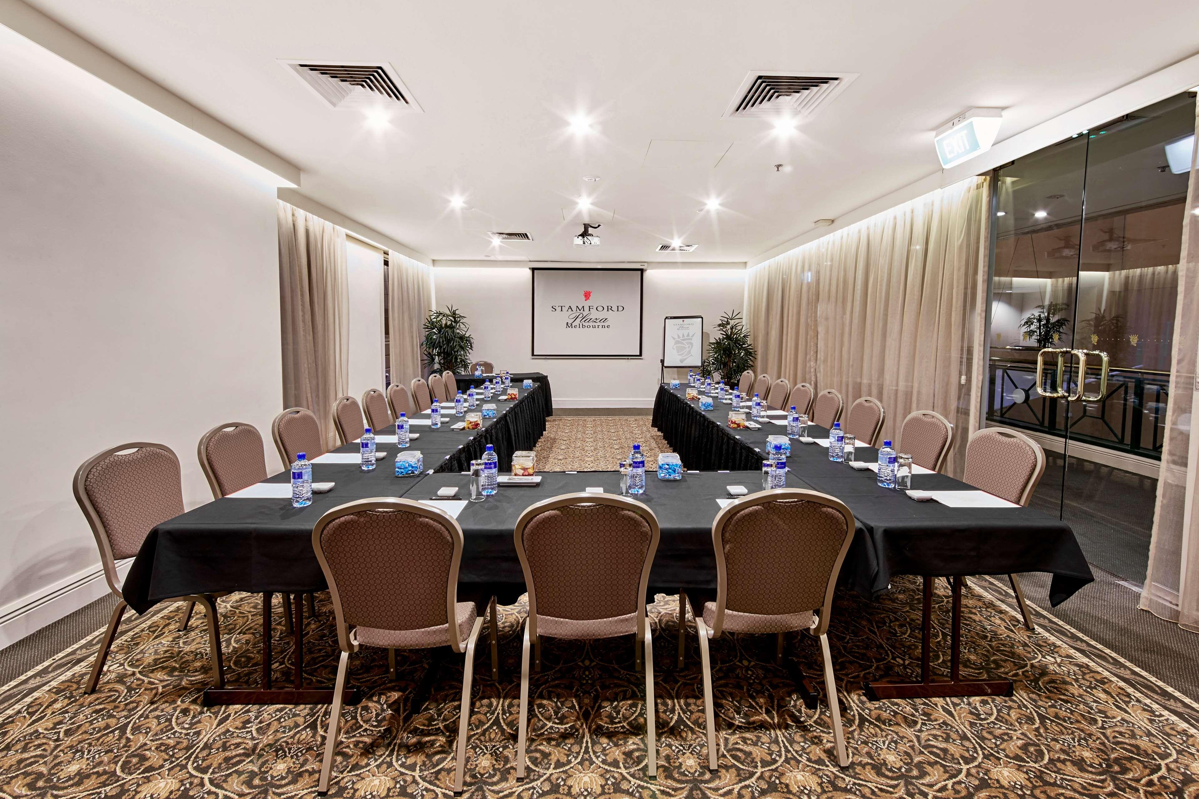 Hotel Stamford Plaza Melburne Exterior foto The photo shows a conference room set up for a meeting. There are several long tables arranged in a U-shape, covered with black tablecloths. Each table has a water bottle and notepad placed at intervals. The room is well-lit, with light-colored walls