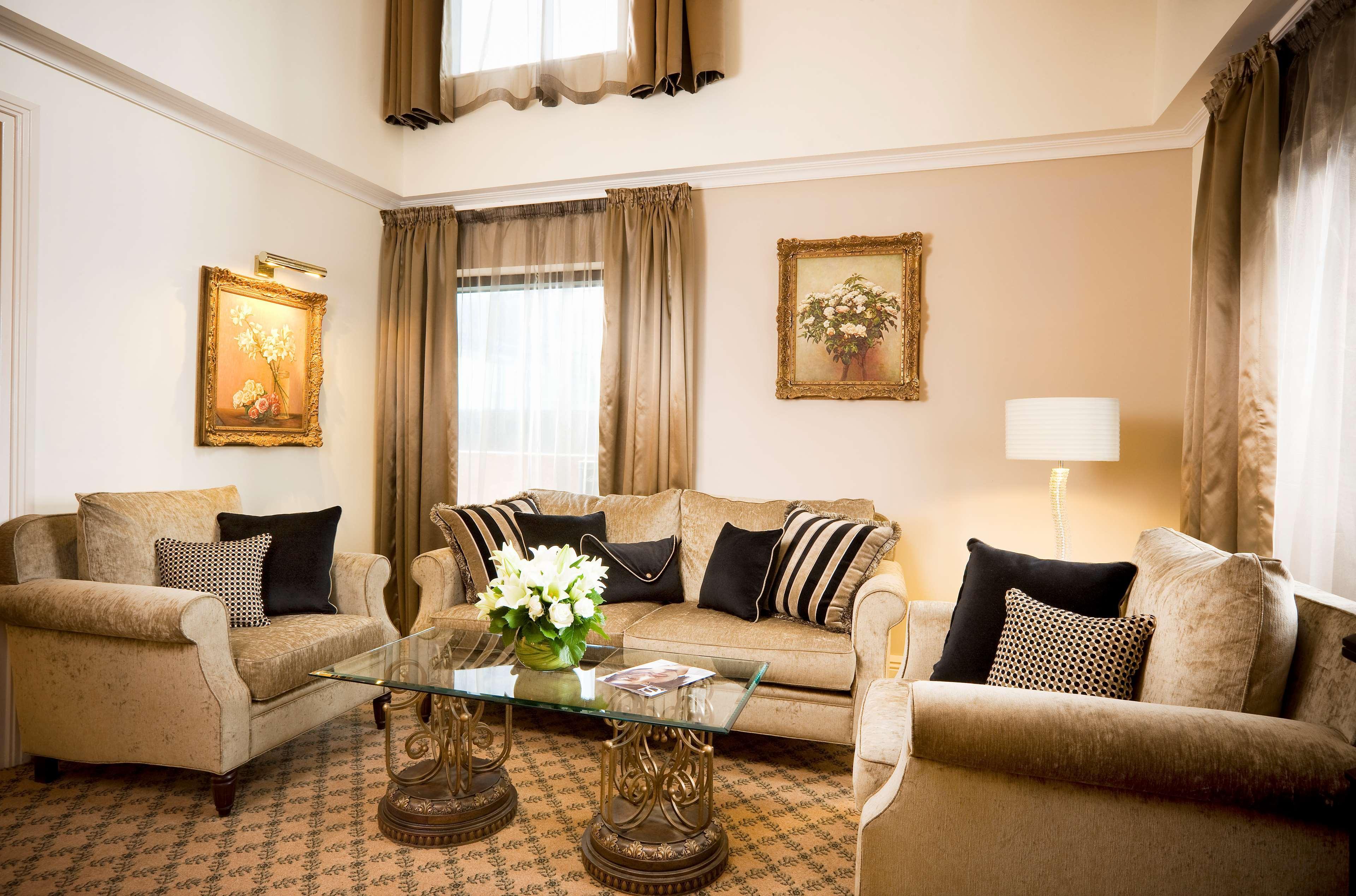 Hotel Stamford Plaza Melburne Habitación foto The photo depicts a stylish living room with a warm and inviting aesthetic. It features a set of comfortable beige sofas adorned with decorative pillows in black and patterned designs. There is a glass coffee table at the center, supported by elegant