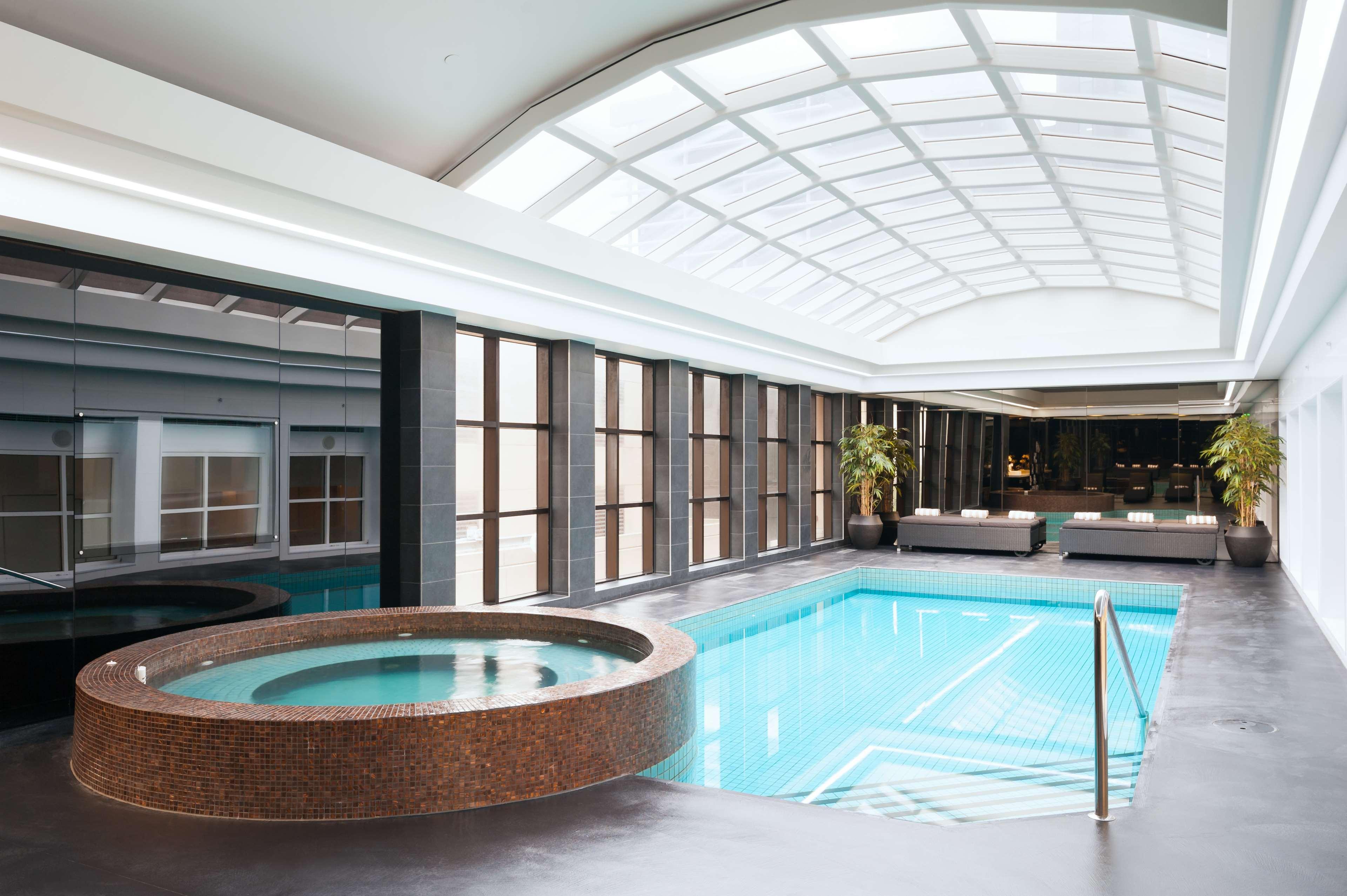 Hotel Stamford Plaza Melburne Exterior foto The photo shows an indoor swimming pool area. The pool is rectangular and has clear blue water, surrounded by a sleek, modern design. On one side, there is a round hot tub made of dark stone. Large windows line the walls, allowing natural light to fi