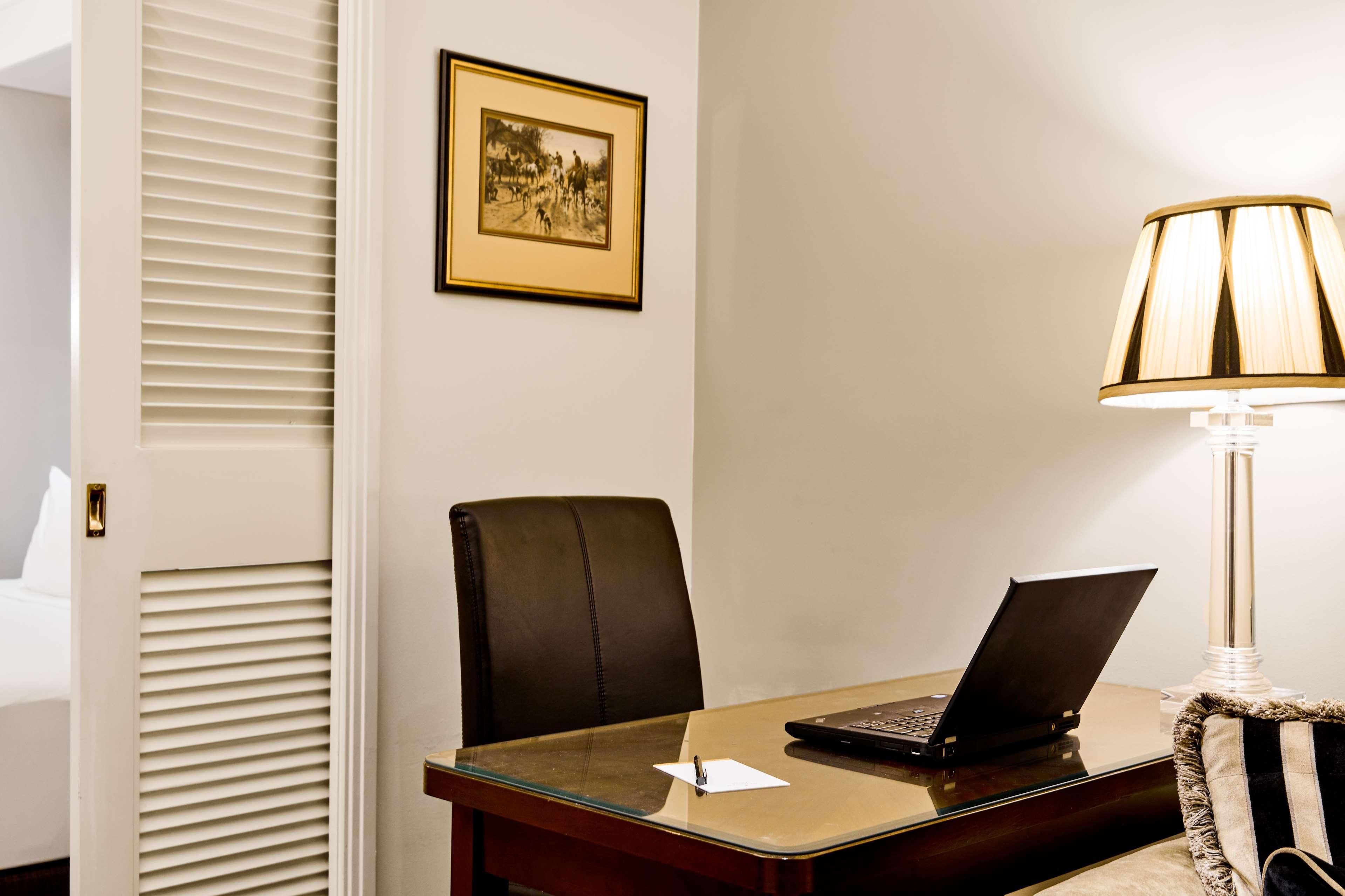Hotel Stamford Plaza Melburne Exterior foto The photo shows a small office or workspace. There is a desk with a glass surface, and on it sits a laptop computer. A piece of paper or notecard is also placed on the desk. Behind the desk is a black office chair. A wall lamp with a striped shade is