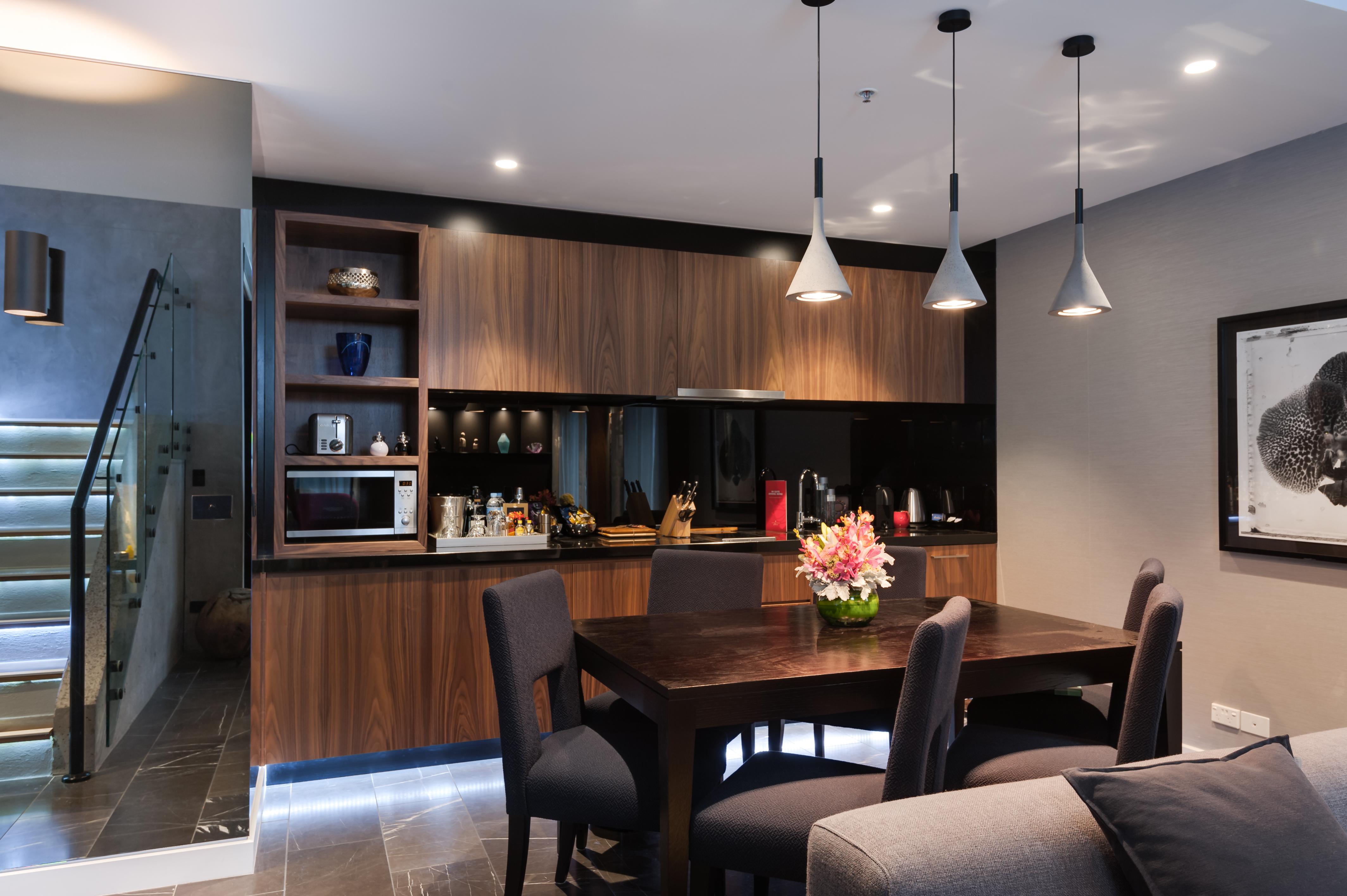 Hotel Stamford Plaza Melburne Exterior foto The image shows a modern kitchen and dining area. The kitchen features dark wooden cabinetry with black accents, a microwave, and various kitchen items arranged on the shelves. There is a dining table made of dark wood, surrounded by several chairs. 