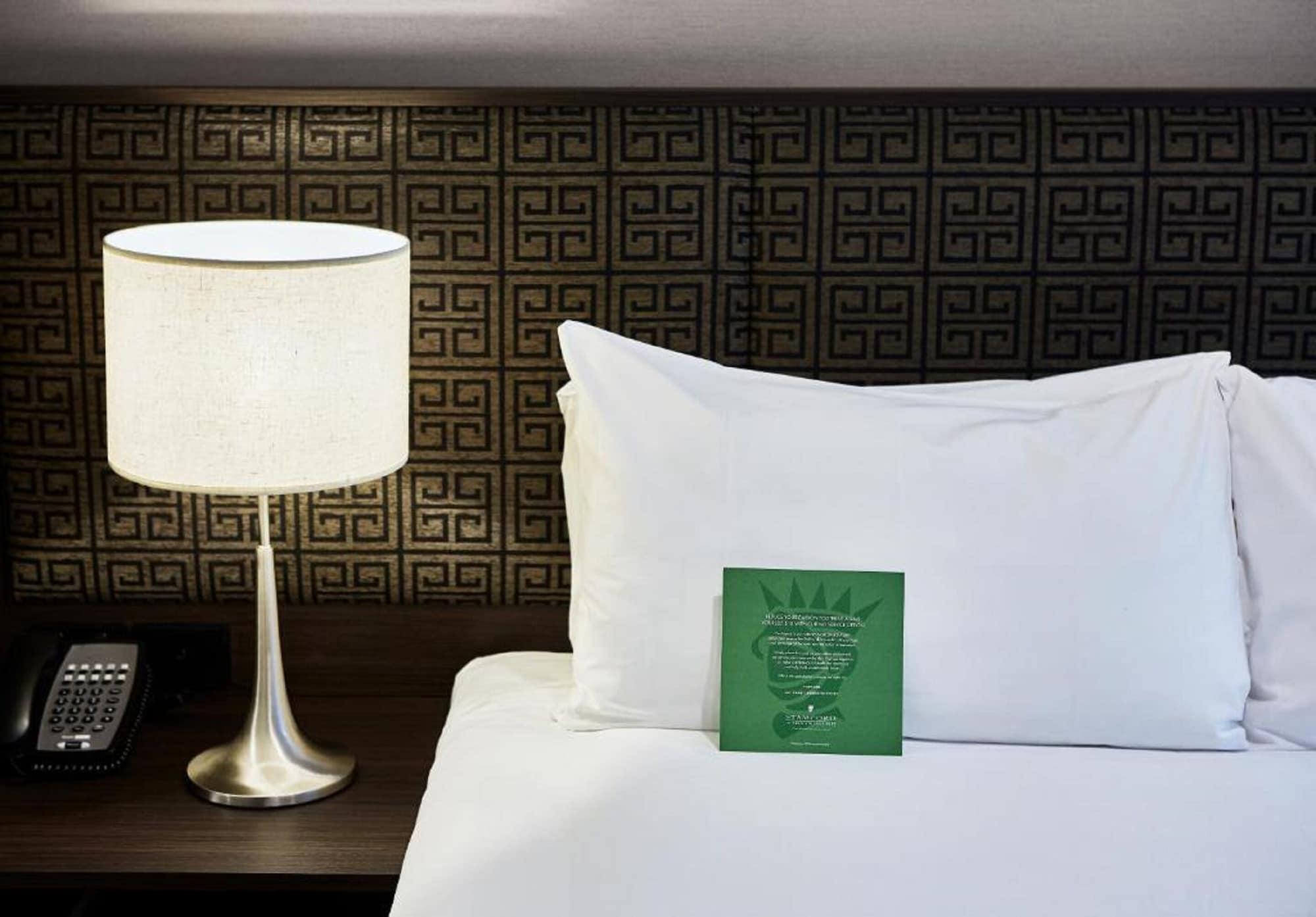 Hotel Stamford Plaza Melburne Exterior foto The photo shows a neatly made bed with a white pillow and a green item placed on top of it. Next to the bed, there is a stylish table lamp with a lampshade that appears to be white. In the background, you can see a patterned wall, which has a geometr