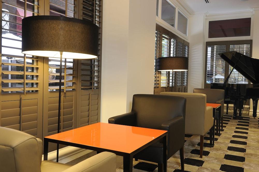 Hotel Stamford Plaza Melburne Exterior foto The photo shows a cozy interior space, likely a lounge or café. It features a modern design with a mix of seating options, including black and light-colored chairs surrounding small tables. One table has a bright orange top, creating a striking visua
