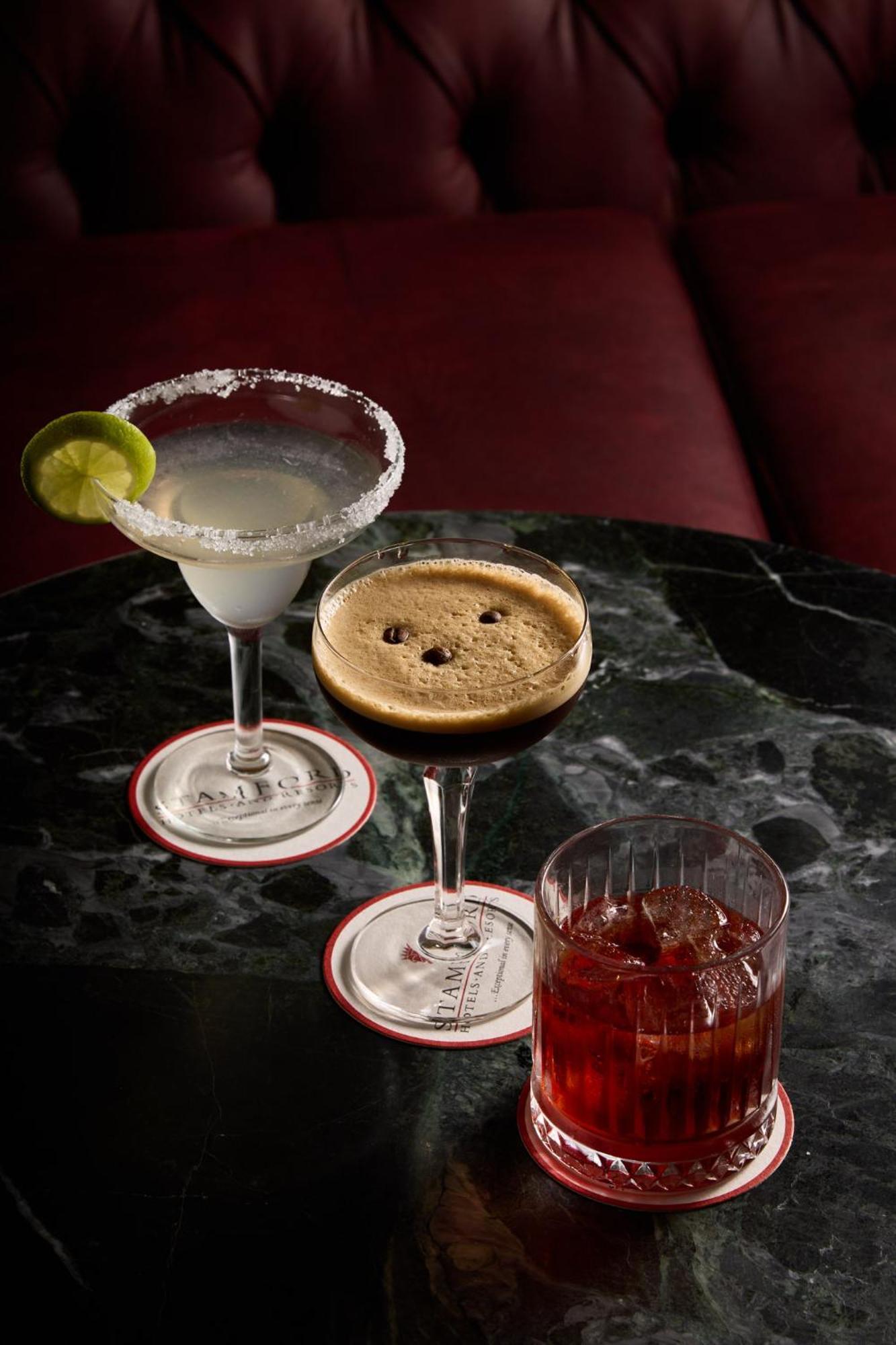 Hotel Stamford Plaza Melburne Exterior foto The photo displays three different cocktails arranged on a dark marble table. 

1. On the left, there is a margarita glass filled with a clear drink, garnished with a lime slice and featuring a salted rim.
2. In the center, a coupe glass holds a dark