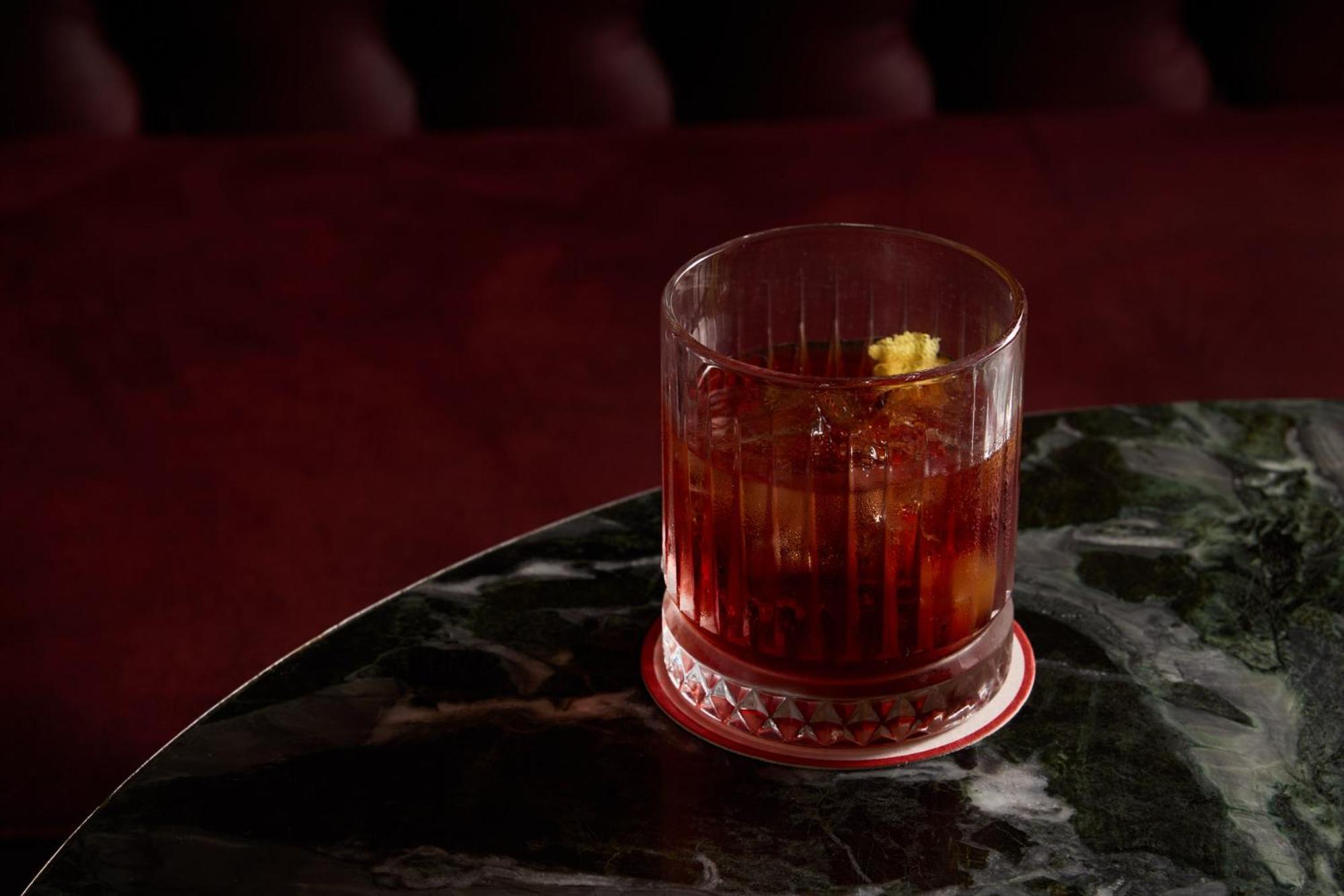 Hotel Stamford Plaza Melburne Exterior foto The photo depicts a short glass filled with a dark-colored beverage, likely an alcoholic drink. The glass has a textured design, with ice cubes visible inside. A twist of lemon peel is perched on the rim, adding a touch of garnish. The drink sits on 