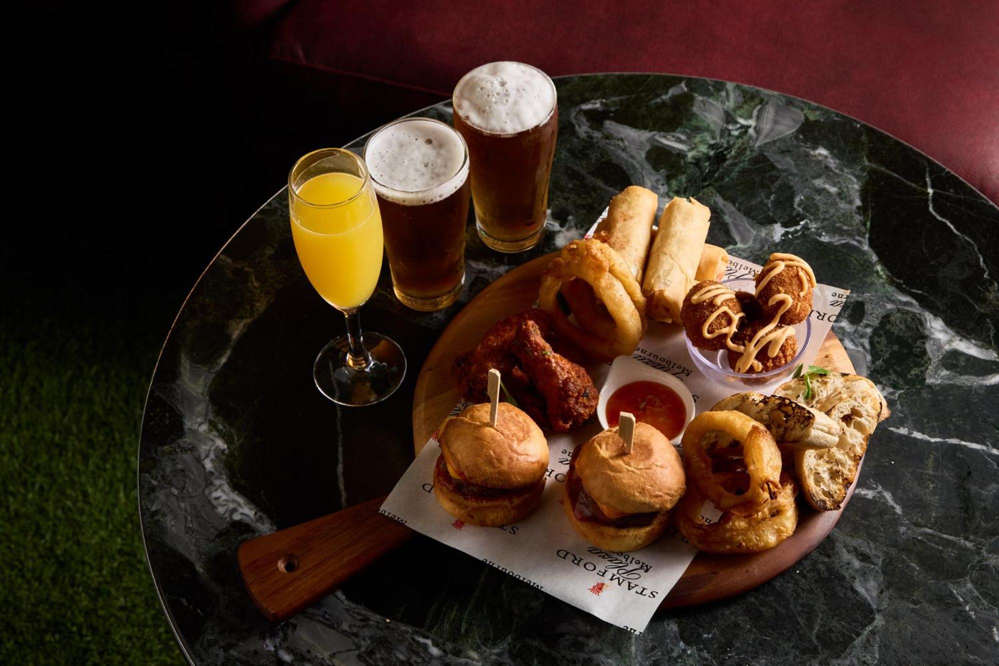 Hotel Stamford Plaza Melburne Exterior foto The photo displays a variety of food and drinks arranged on a marble table. There are small burgers garnished with skewers, crispy chicken pieces, and deep-fried snacks. Additionally, there are two glasses of beer and a cocktail, likely a mimosa, pre