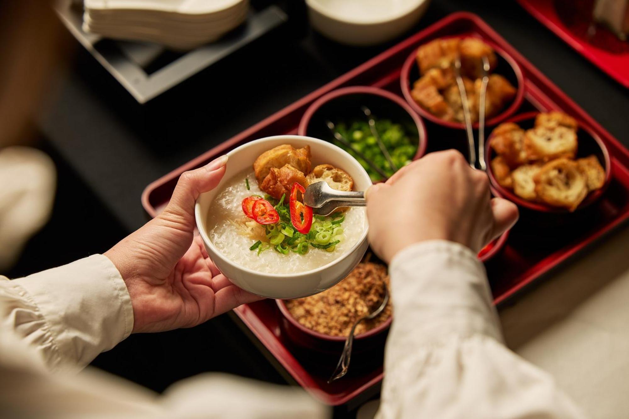 Hotel Stamford Plaza Melburne Exterior foto The photo shows a person serving food from a tray filled with various dishes. In one hand, they are holding a bowl filled with a creamy, likely rice-based dish topped with slices of chili and possibly fried tofu or other toppings. Surrounding the bow