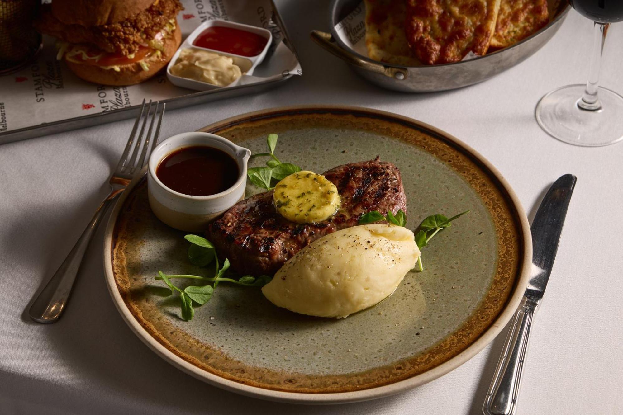 Hotel Stamford Plaza Melburne Exterior foto The photo shows a well-presented plate featuring a serving of steak, topped with a dollop of herb butter and surrounded by fresh sprouts or microgreens. There is a smooth portion of mashed potatoes beside the steak, and a small bowl of sauce, likely 