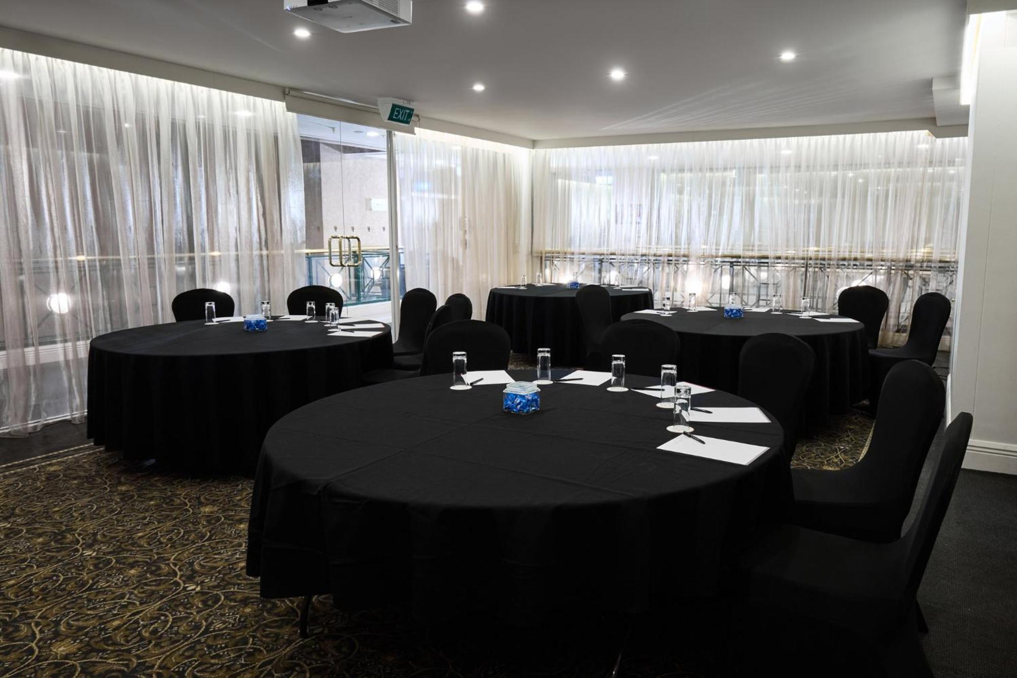 Hotel Stamford Plaza Melburne Exterior foto The photo shows a meeting or conference room set up with several round tables covered in black tablecloths. Each table is accompanied by black chairs. There are some white notepads and pens placed on the tables, and a small decorative item, possibly 