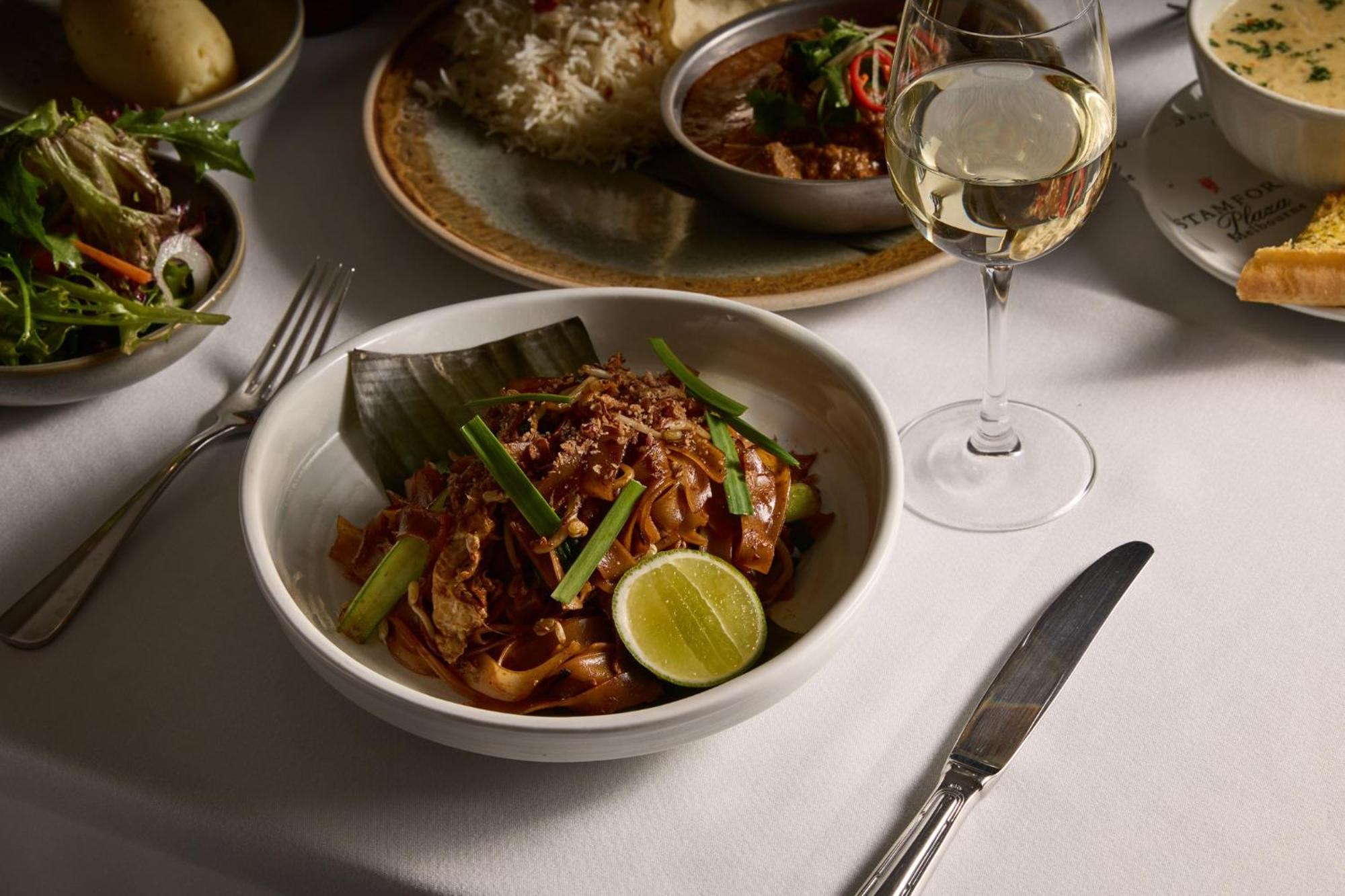 Hotel Stamford Plaza Melburne Exterior foto The photo features a beautifully arranged dining table with several dishes. In the foreground, there is a bowl of noodles topped with green onions and garnished with a lime wedge. The noodles appear to be stir-fried and have a rich color. Next to the